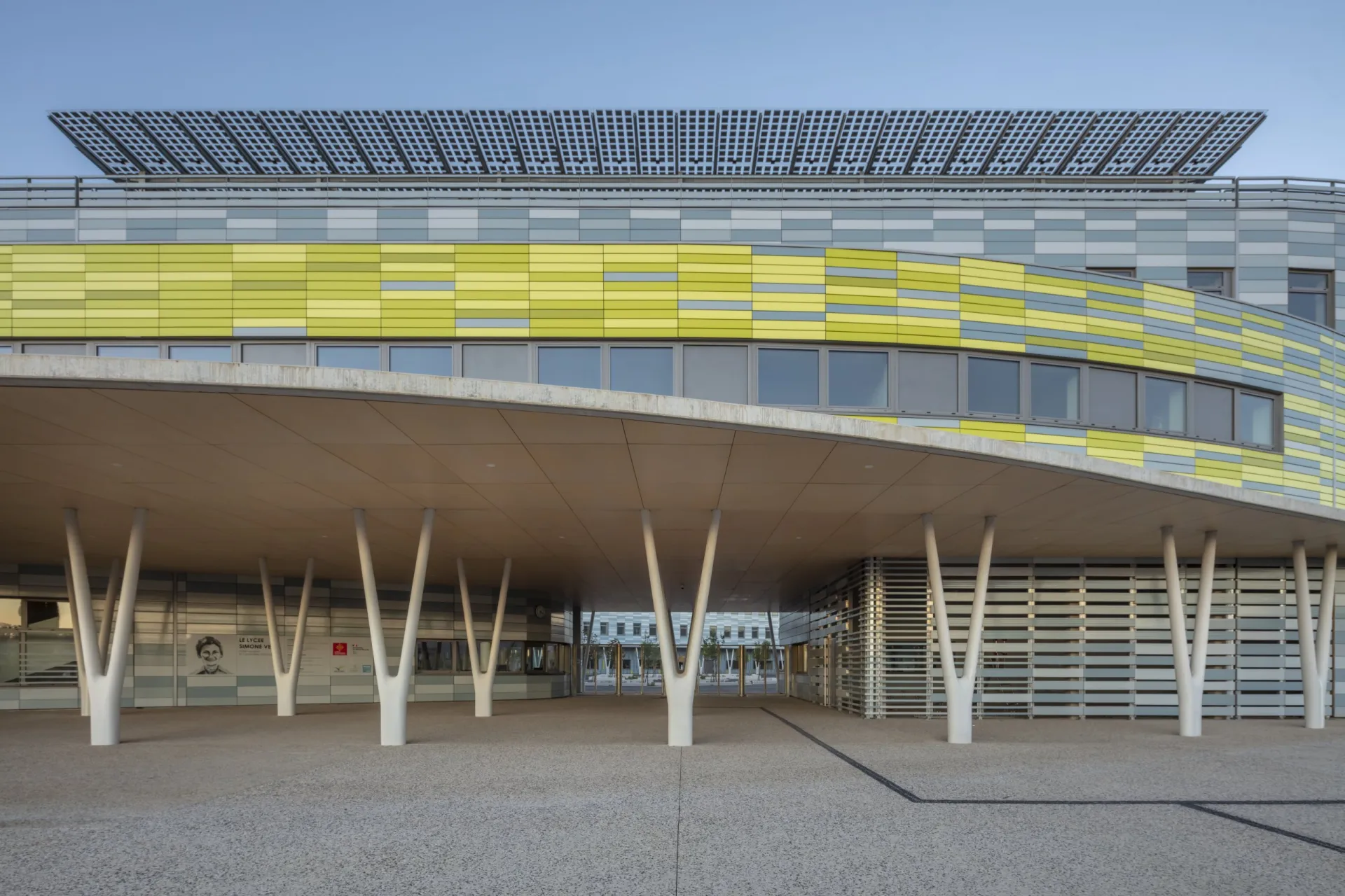 Gymnasium Simone Veil in Gignac: geschwungenes Vordach auf V-förmigen UHPC-Stützen, Fassade mit gelb-grauer Verkleidung